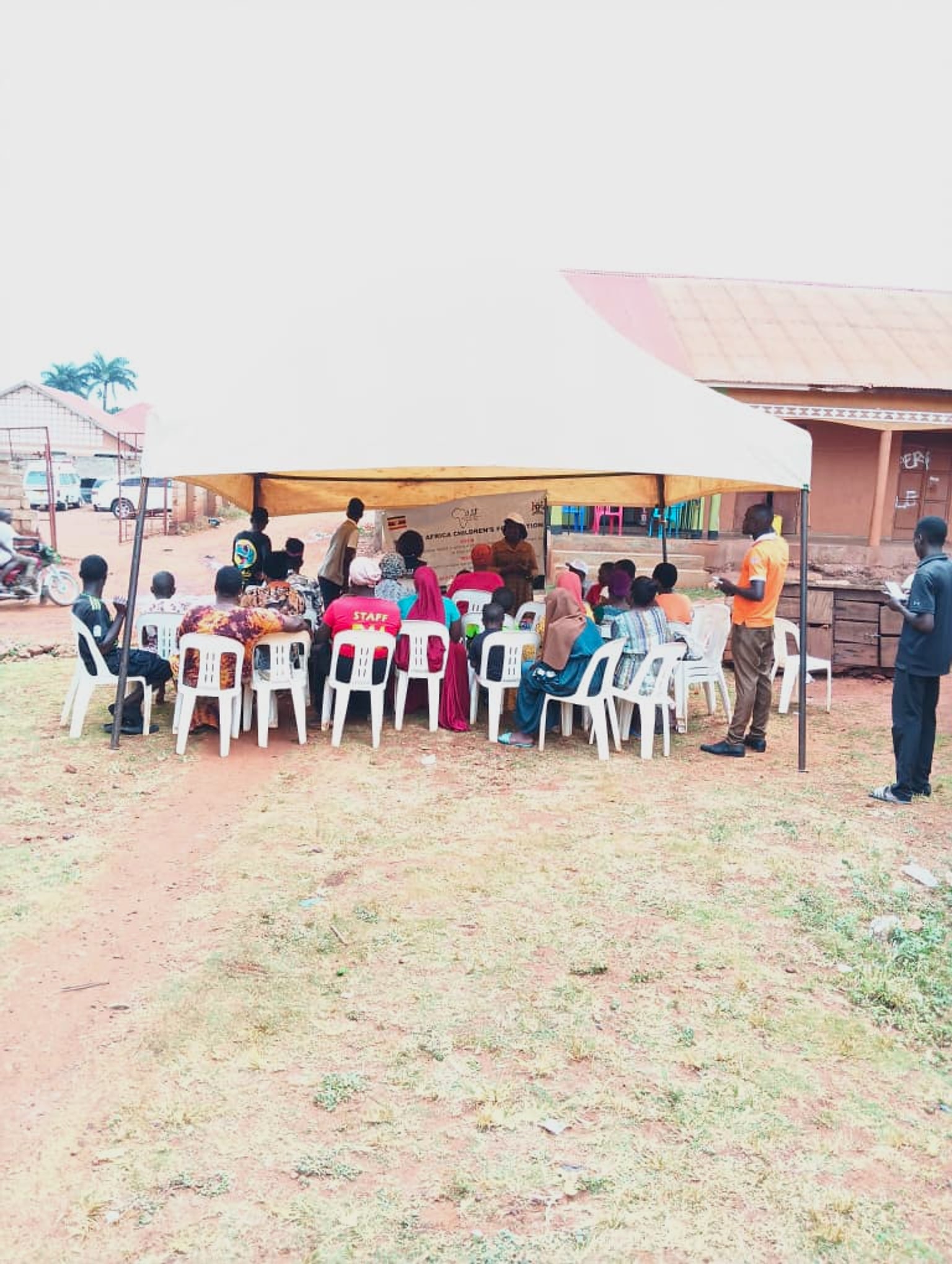 Children, caregivers and the foundation team gathered under a tent outside the Bugembe office